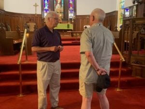 two men in a church with red carpet facing each other